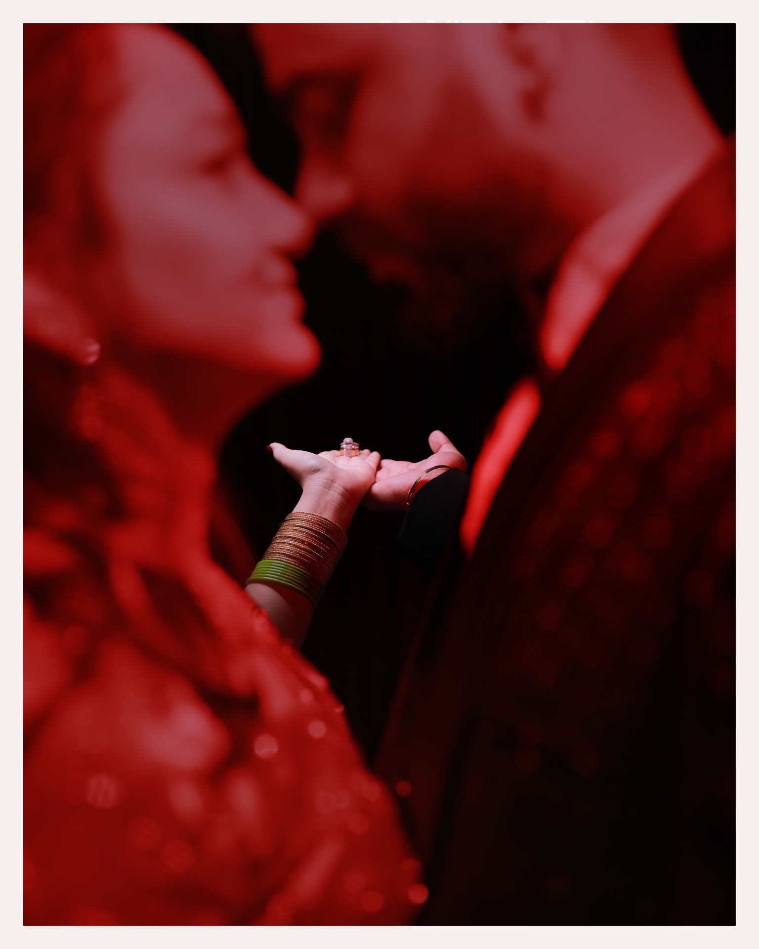 The couple's hands holding the ring under red light